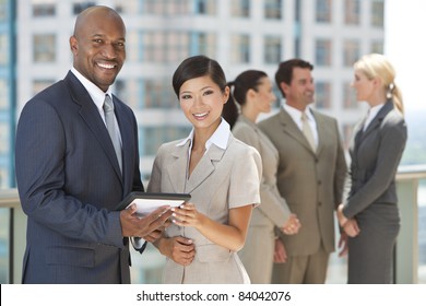 African American Businessman And Chinese Asian Businesswoman Using Tablet Computer With Interracial Group Of Business Men & Women Team.