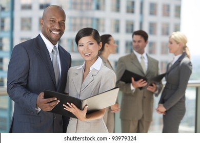 African American Businessman And Chinese Asian Businesswoman Using A Black Folder With Interracial Group Of Business Men & Women Team.