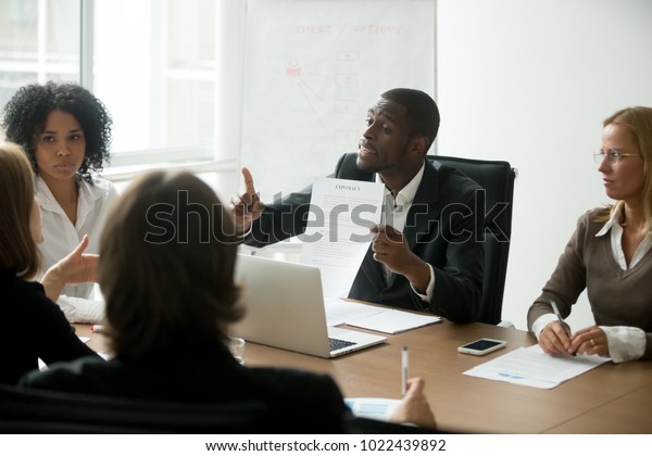 African american businessman disagreeing with\
contract terms at group multi-ethnic negotiations, black partner\
arguing about deal conditions or fraud scam pointing at document at\
multiracial meeting