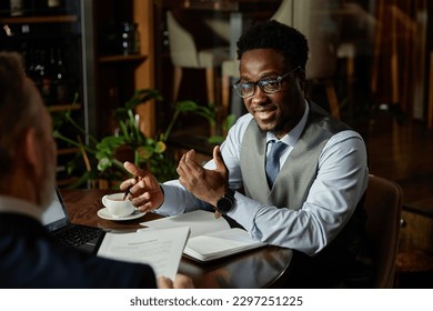 African American businessman discussing business plans with his partner while they sitting at table at meeting in cafe - Powered by Shutterstock