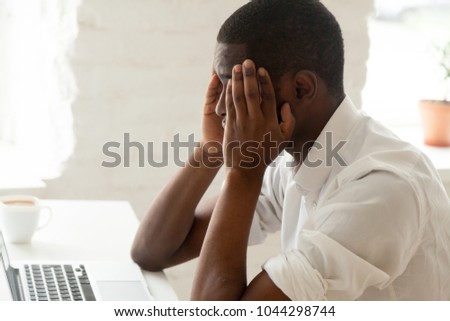 African american businessman feeling headache migraine at work touching temples, stressed tired upset black man feeling dizzy or depressed and frustrated while working on laptop in office, side view