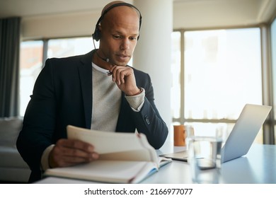 African American businessman going through paperwork during conference call via laptop in the office. - Shutterstock ID 2166977077