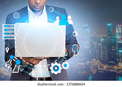 African American Businessman Holding Laptop With GUI Interface Over Night City Background. Concept Of Hi Tech In Business. Double Exposure