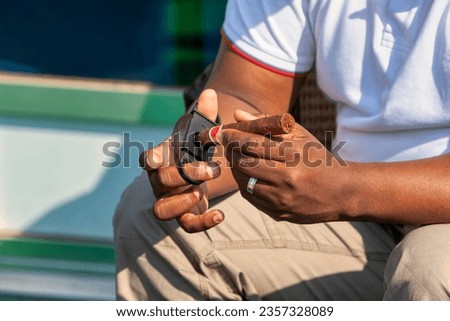 african american businessman sited outdoors using a Guillotine cigar cutter to cut a premium cigar