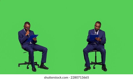 African american businessman taking notes on files, thinking about new corporate ideas over greenscreen backdrop. Male entrepreneur writing business information on papers, sitting on chair. - Powered by Shutterstock