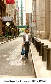African American Businessman Traveling, Working In New York. Young Black Man Walking On Narrow Old Street With High Buildings, Carrying Blue Bag. Car Running On Background. Color Filtered Effect.
