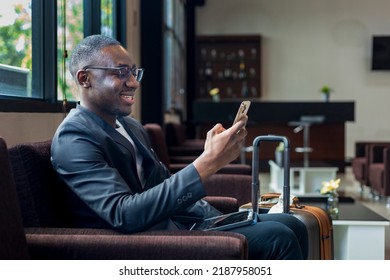 African American businessman is using mobile phone for video call while waiting in airline business departure lounge waiting for boarding airplane - Powered by Shutterstock