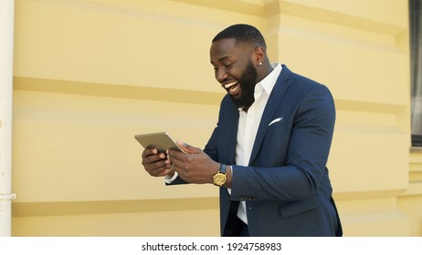 African American Businessman Walking With Tablet Computer Outdoors. Happy African Business Man Getting Good Results On Tablet Outside. Successful Afro Guy Making Yes Gesture On Urban Street.