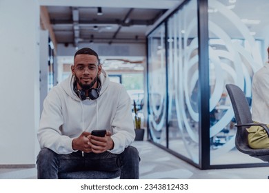 African American businessman wearing headphones while using a smartphone, fully engaged in his work at a modern office, showcasing focus, productivity, and contemporary professionalism - Powered by Shutterstock