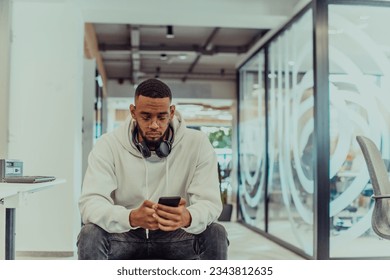 African American businessman wearing headphones while using a smartphone, fully engaged in his work at a modern office, showcasing focus, productivity, and contemporary professionalism - Powered by Shutterstock
