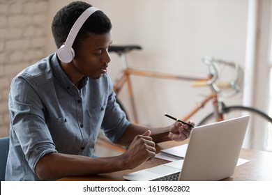 African American businessman wearing headset using laptop, working online, manager consulting client customer, making video call, trainee intern watching webinar, writing notes, listening to lecture