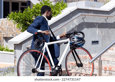 African american businessman wearing suit holding bicycle on stairs. On the go, commuting and office concept. - Powered by Shutterstock