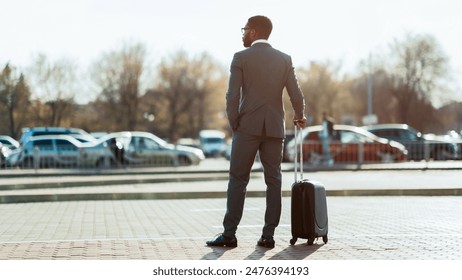 African American businessman wearing suit with suitcase crossing street, going vacation, back view, looking at copy space, panorama - Powered by Shutterstock