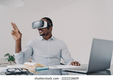 African american businessman wearing vr glasses working on project in cyberspace at laptop. Black male manager works in augmented virtual reality, using high tech gadget for business at the workplace. - Powered by Shutterstock