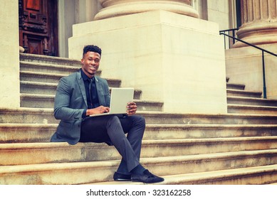 African American Businessman Working In New York. Wearing Fashionable Jacket, Necktie, Young Black Man Sitting On Stairs Outside Office Building, Smiling, Working On Laptop Computer. Instagram Effect.