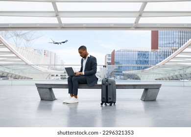 African American Businessman Working On Laptop While Waiting Flight At Modern Airport, Young Black Male In Suit Using Computer, Andswering Emails While Sitting On Bench At terminal Hall, Copy Space - Powered by Shutterstock