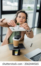 African American Businesswoman With Funny Grimace Making Pyramid From Flowerpot, Stationery And Paper Cup On Desk