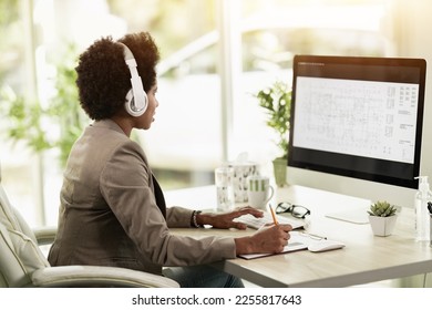 African American businesswoman with headphones checking project and planning on the internet while sitting at computer in an office alone at work. - Shutterstock ID 2255817643