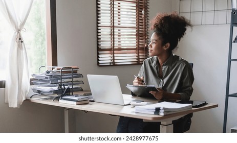 African american businesswoman looking outside window while writing notes and thinking new business. - Powered by Shutterstock