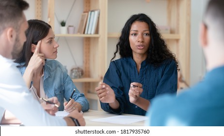African American businesswoman mentor coach speaking, training staff at meeting, sitting at table in boardroom, female employee sharing ideas, discussing project strategy with colleagues