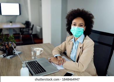 African American businesswoman with protective face mask working on a computer at her office desk and looking at camera. 