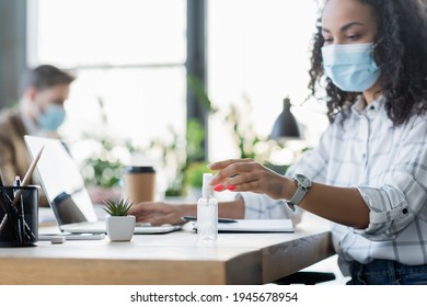 african american businesswoman in protective mask near hand sanitizer and laptop at workplace - Powered by Shutterstock