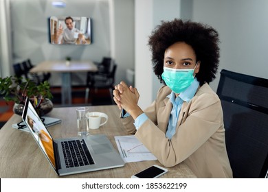 African American Businesswoman Using Computer And Having Conference Call While Wearing Face Mask In The Office Due To Coronavirus Pandemic. 