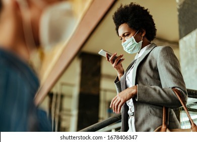 African American Businesswoman Wearing Face Mask While Using Voice Assistant On Mobile Phone At Public Train Station. 