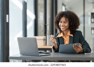 African american businesswoman working with laptop looking at financial information Successful business results in modern office with happy note taking in folder. - Powered by Shutterstock