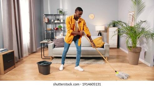 African American Busy Handsome Young Guy Washing Floor In Modern Living Room Doing Housework, Male Cleaning House Parquet Using Mop Keeping Home Clean, Housekeeper, Everyday Life, Routine Concept