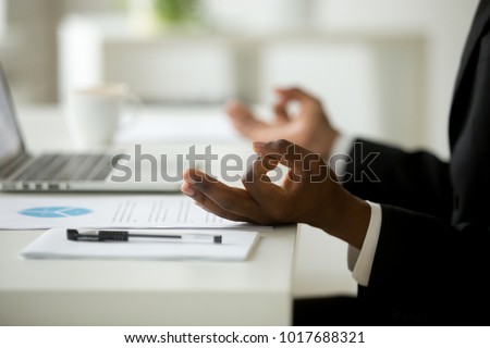 African american calm businessman relaxing meditating in office, peaceful ceo in suit practicing yoga at work, focus on black man hands in mudra, successful mindful people habits concept, close up