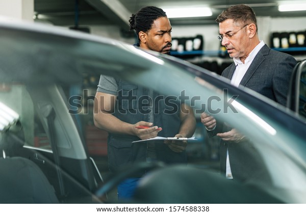 African American car mechanic talking to a businessman\
in auto repair shop. 