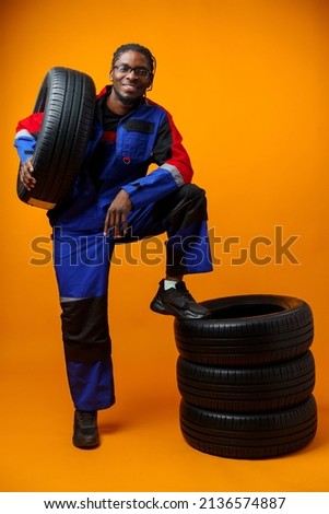 African american car service worker with car tyre against yellow background