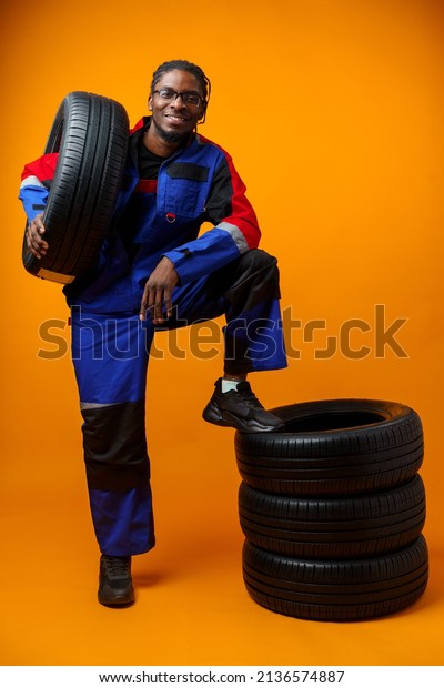 African american car service worker with car\
tyre against yellow\
background