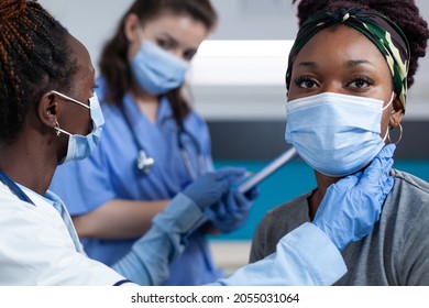 African American Cardiologist Doctor Mesauring Cardiac Pulse While Therapist Nurse Writing Medical Treatment During Clinical Examination In Hospital Office. Women Wearing Face Mask Against Coronavirus