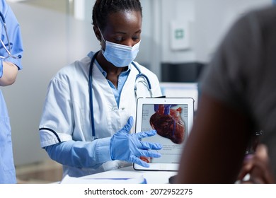 African American Cardiologist Doctor Showing Heart Radiohraphy To Sick Patient Using Tablet Explaining Medication Treatment During Clinical Appointment In Hospital Office. People With Medical Face