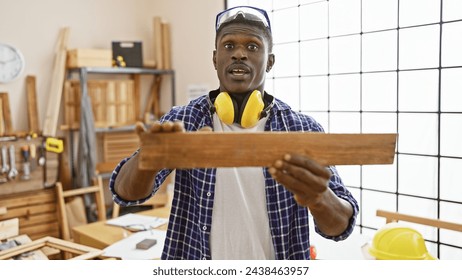 African american carpenter examines wood in a well-lit workshop wearing safety gear. - Powered by Shutterstock