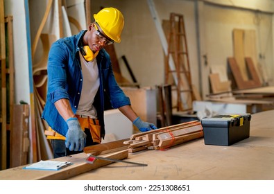 African American carpenter man use measure tape to check and work with timber in factory workplace and tools box is place on table near working area. - Powered by Shutterstock