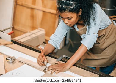 African American carpenter woman drawing a line on wood with a pencil and ruler in workshop. Focused on precise measurements, woodworking, and construction tasks in carpentry, National Carpenters Day - Powered by Shutterstock