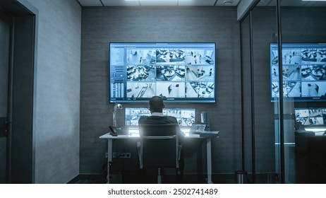 African American CCTV operator works with security cameras on computer and tablet in dim monitoring center, talks on walkie talkie. Surveillance footage on multiple monitors and big digital screen. - Powered by Shutterstock