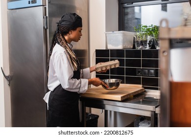 African American Chef In Apron Holding Egg Carton And Bowl In Kitchen