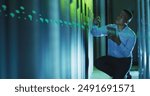 African American chef holding tablet, examining server racks. He has short black hair, wearing light blue shirt