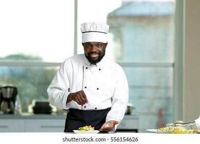 African American Chef Salting Tasty Salad In Kitchen