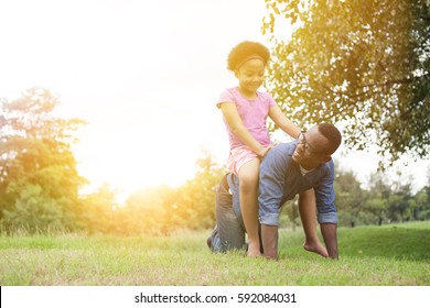 African American child riding on father's back in the park during sunset with copyspace