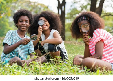 African American children sitting in the grass and looking through the magnifying glass between learn beyond the classroom. 
Education outdoor concept. - Powered by Shutterstock