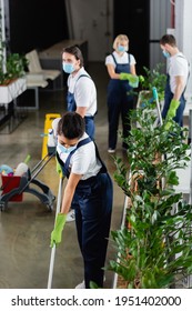 African American Cleaner In Medical Mask Holding Mop Near Plants In Office