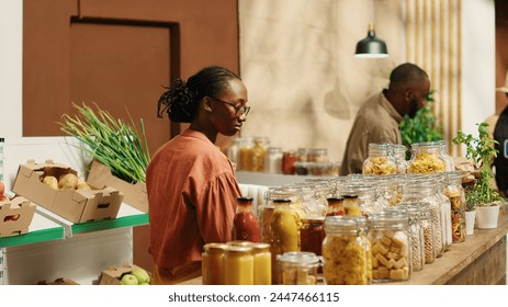 African american client examines bio homemade bulk products, looking to buy natural ethically sourced food alternatives for healthy nutrition. Woman shopping for goods at zero waste store. Camera 1. - Powered by Shutterstock