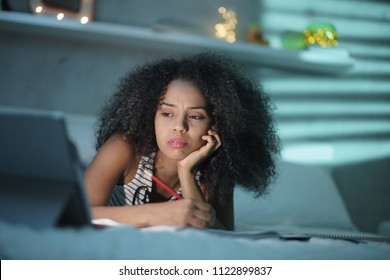 African American College Student Doing Homework. Young Black Woman Preparing School Test In Bedroom With Laptop Computer At Night, Lying On Bed