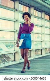 African American College Student Studies In New York. Wearing Long Sleeve T Shirt, Denim Skirt, Shoulder Carrying Bag, Holding Laptop Computer, Girl Walks On Campus, Talks On Phone. Filtered Effect.