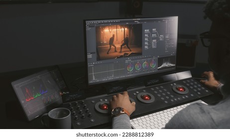 African American colorist makes color grading on control machine in modern studio. Big screens with action film footage and RGB colour correction graphic bar on the wall. Film post production process. - Shutterstock ID 2288812389